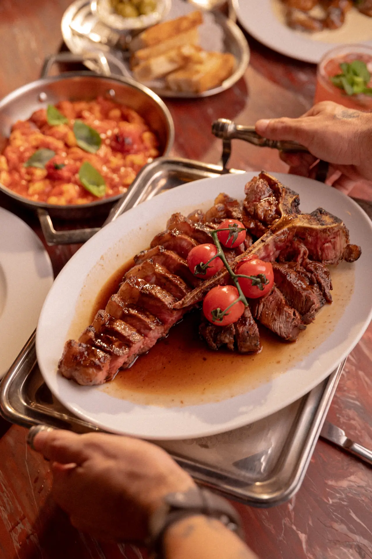 Carne fatiada com tomates sendo servida numa mesa farta