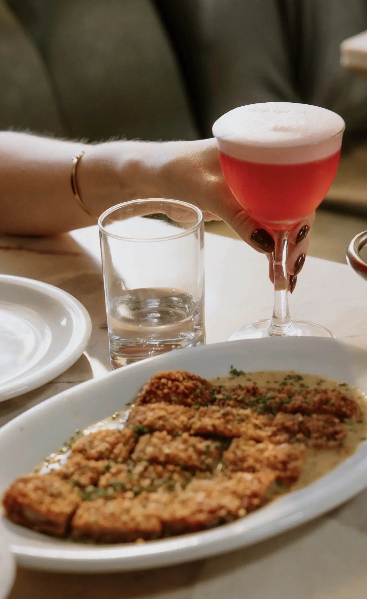 Drink rosado com espuma ao lado de um prato à milanesa