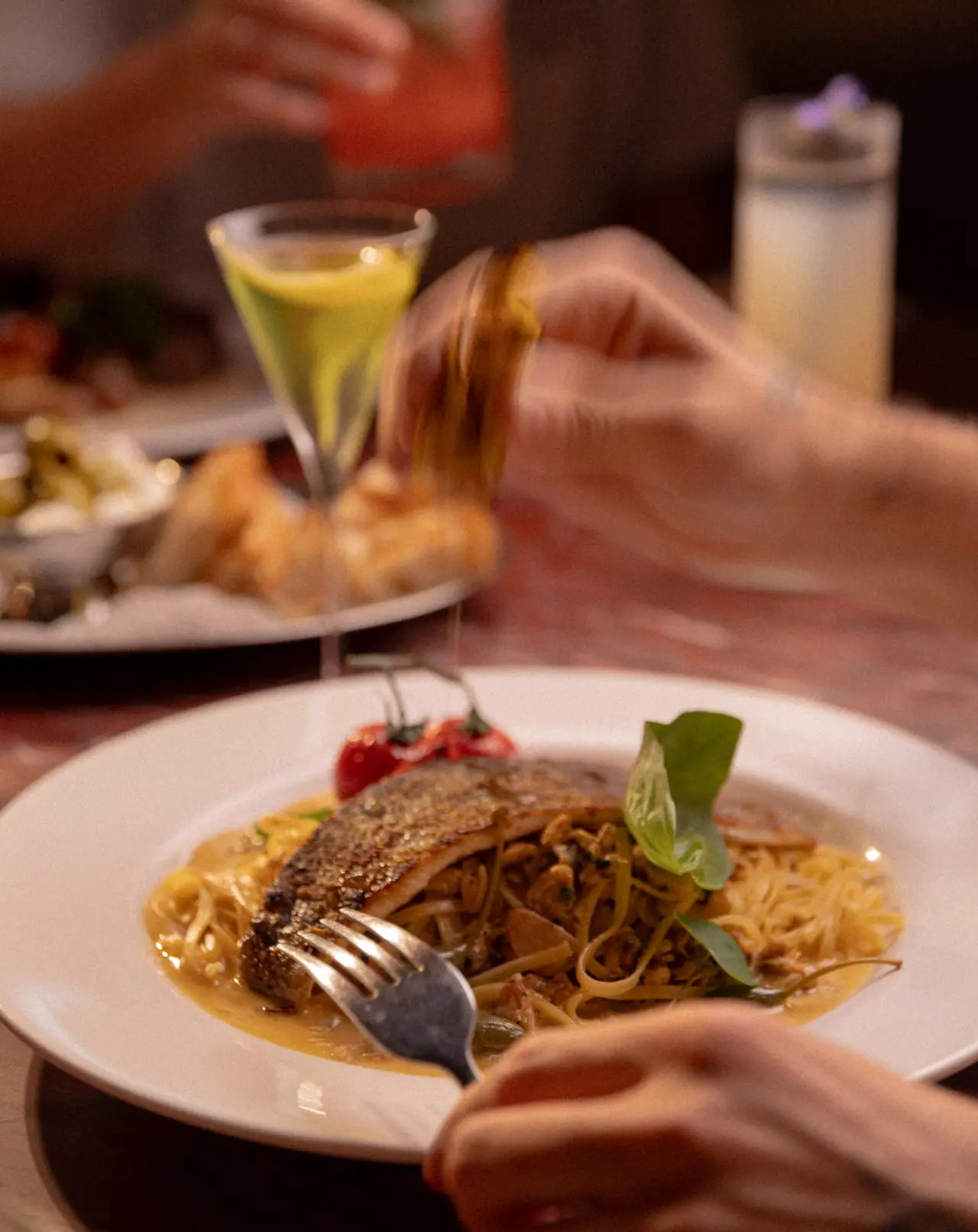 Prato de massa com peixe e uma taça de drink sendo servida