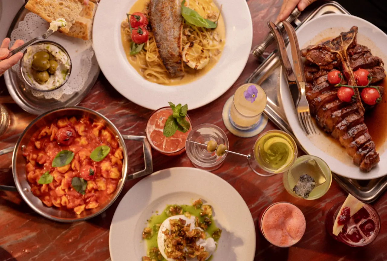 Mesa vista de cima com antepastos, massas e drinks sendo divididos
