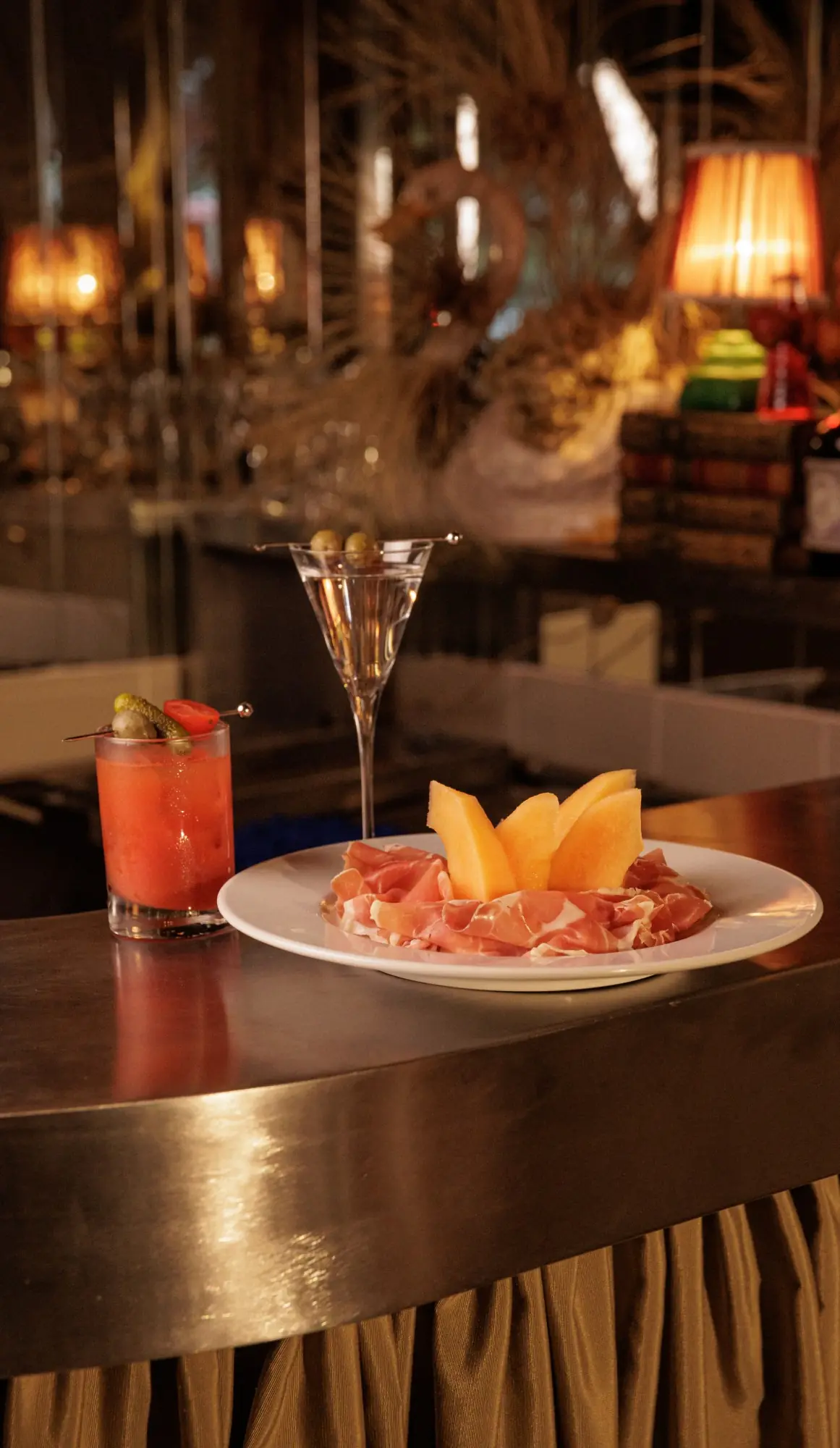 Presunto cru com melão, drink de tomate e martíni sobre o balcão do bar